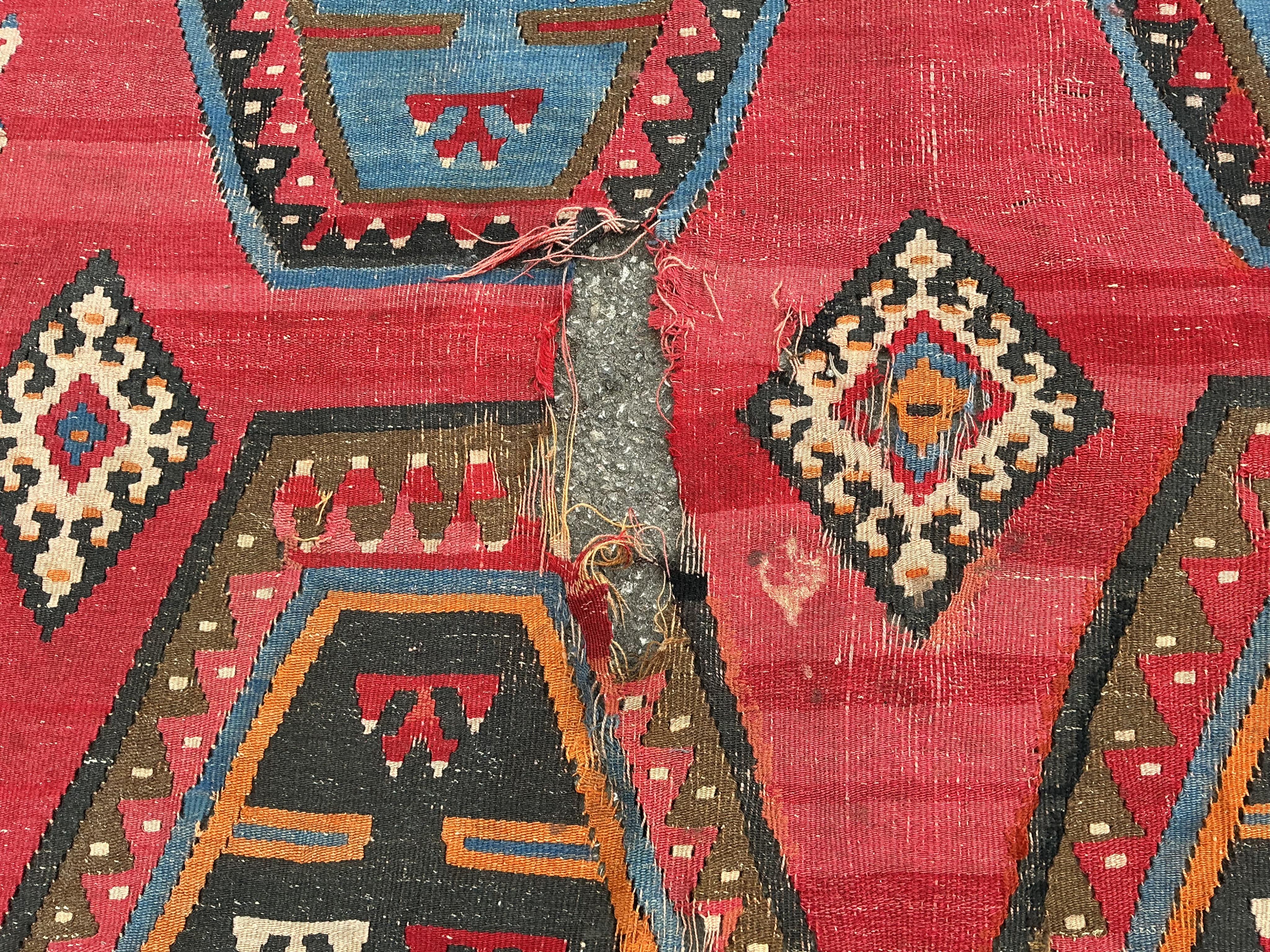 A Turkish Kilim flatweave polychrome carpet, woven with three rows of hexagons, on a red ground, (severely holed and damaged in places), 373 x 267cm